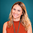 Smiling headshot of woman with wavy blonde hair, rust top and teal background